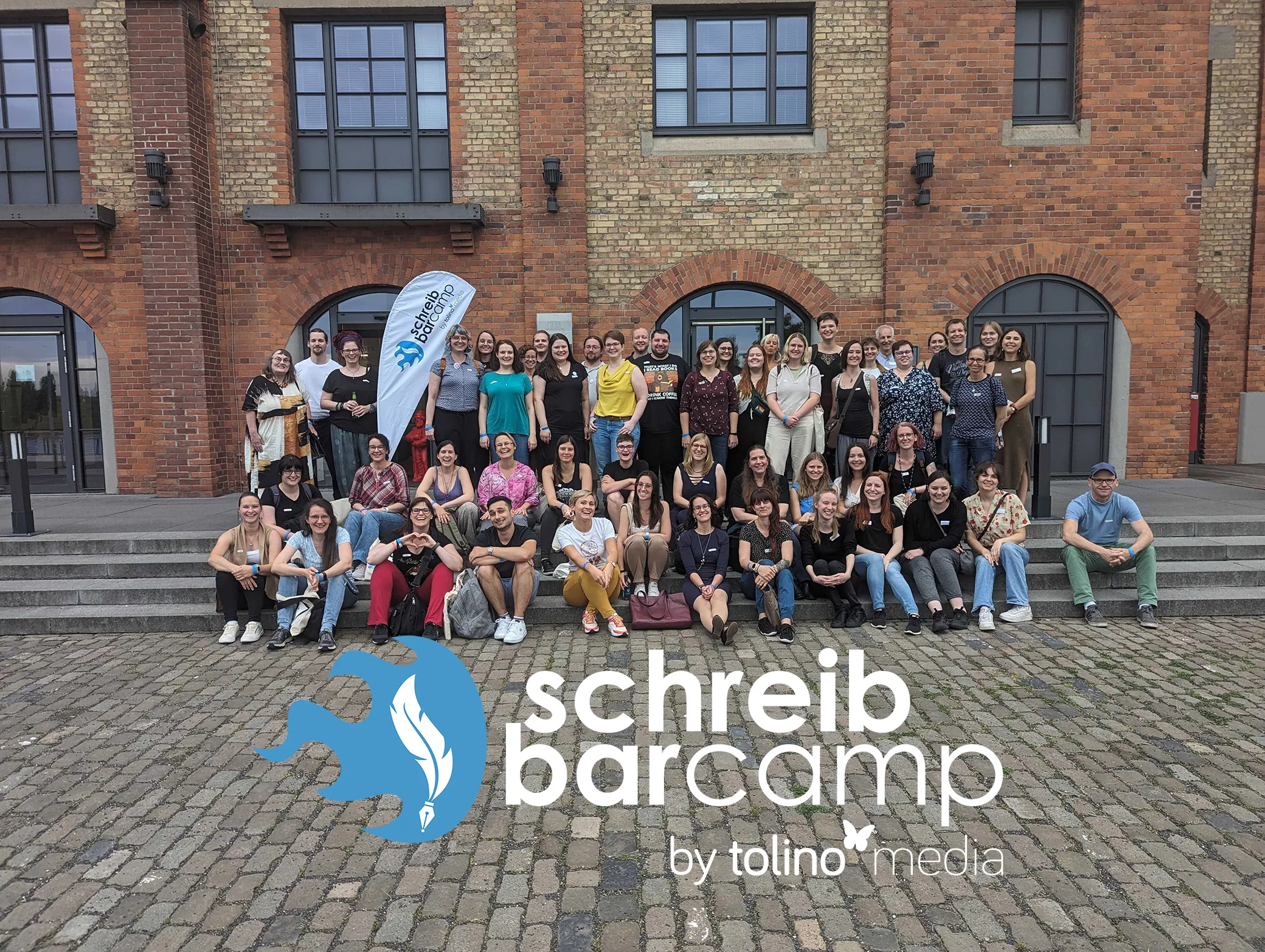 Gruppe von Menschen vor einem Backsteingebäude mit Banner des SchreibBarCamps